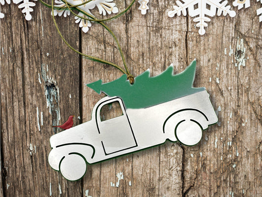 holiday ornament made of stainless steel holding a green Christmas tree in the back. A red bird sits on the hood of the truck.