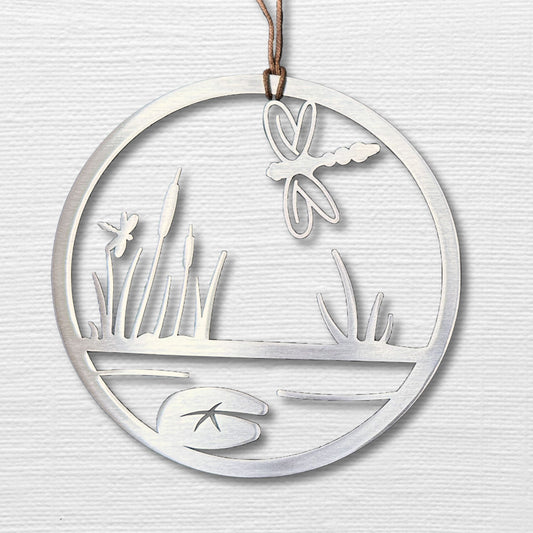 a circular metal ornament with a lake and a dragonfly