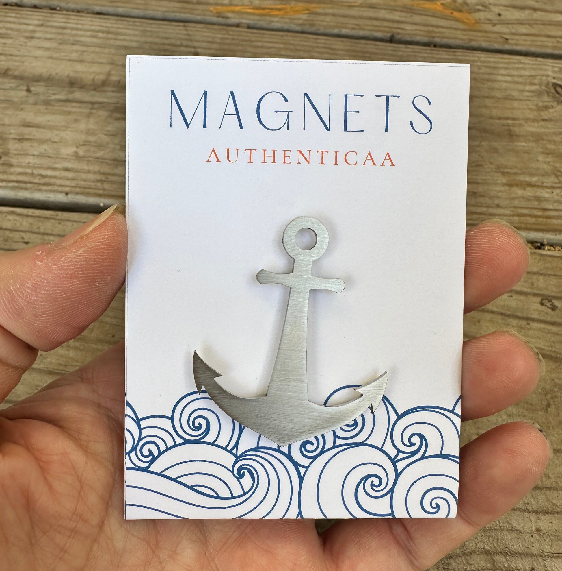 Anchor magnet made of stainless steel placed on an illustrated eco friendly card. Held in hand